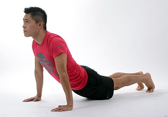 Asian man performing yoga cobra pose in red shirt