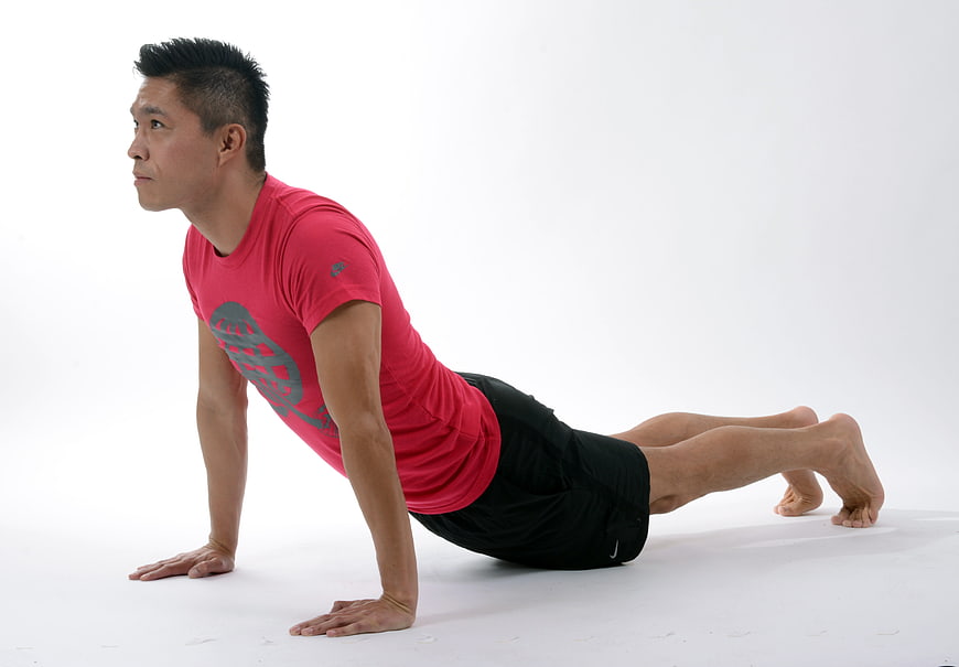 Asian man performing yoga cobra pose in red shirt