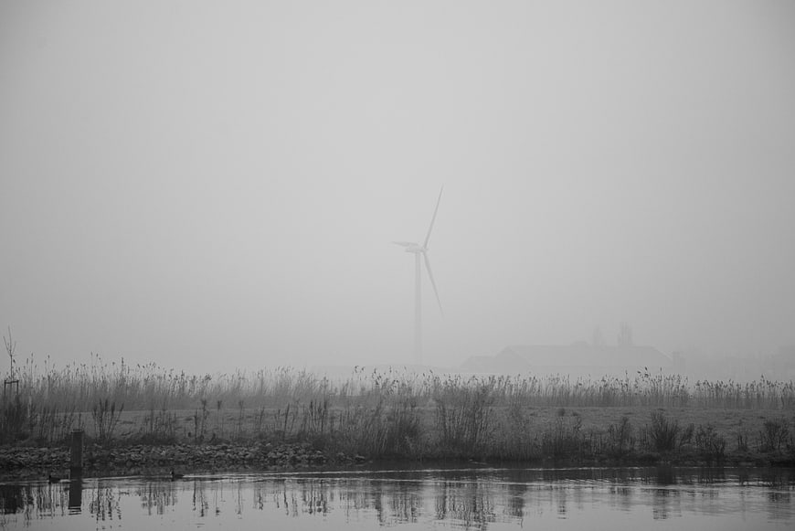Lone wind turbine in foggy landscape with water reflection