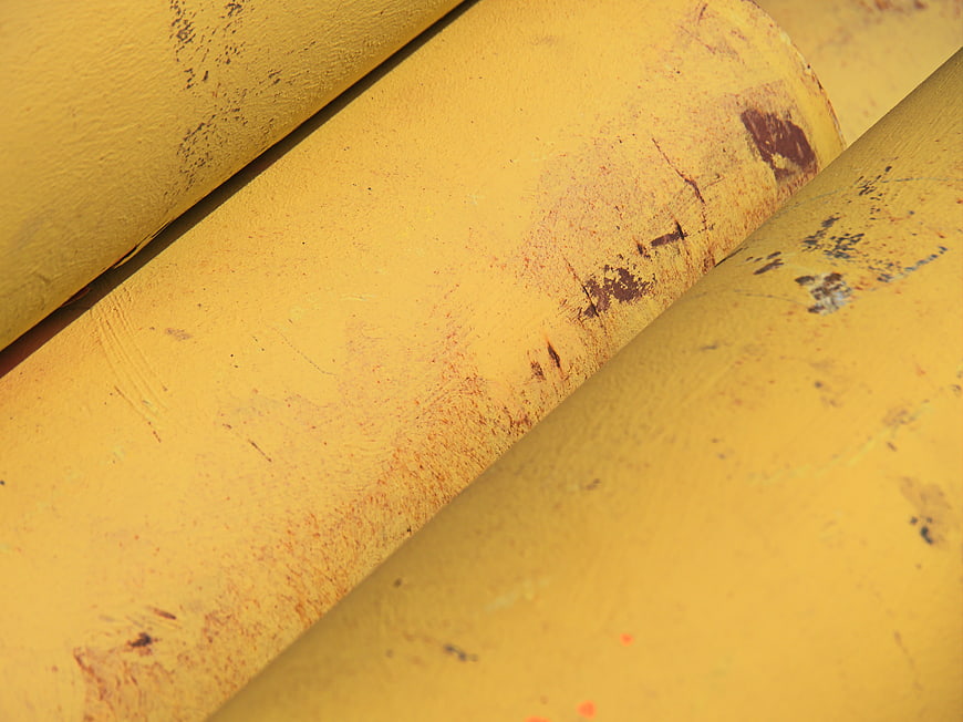 Close-up of weathered yellow industrial pipes with rust texture