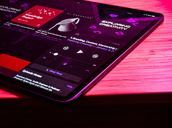 Tablet displaying podcast app on wooden desk with neon lighting