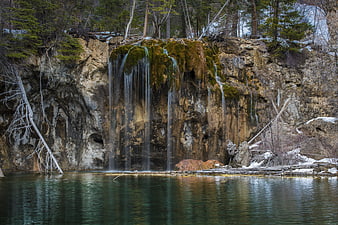 Frozen waterfall cascading over mossy cliff into calm lake