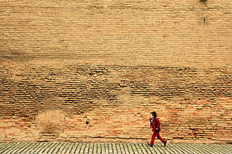 Child in red running past a massive textured ancient brick wall