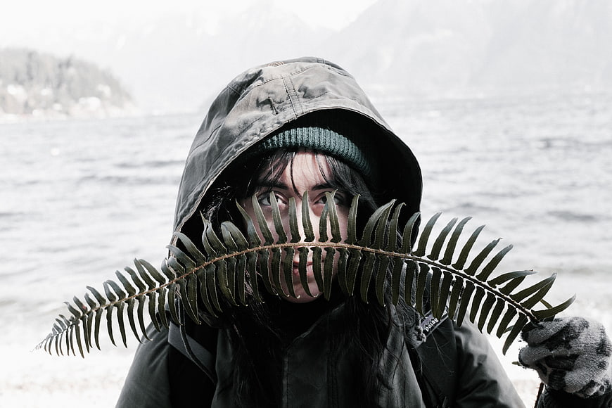 Woman in Hoodie Holding Fern Leaf by Lake