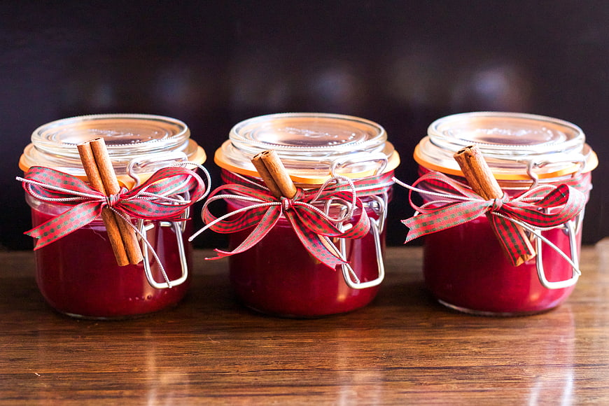 Three jars of homemade cranberry jam with cinnamon sticks and ribbons