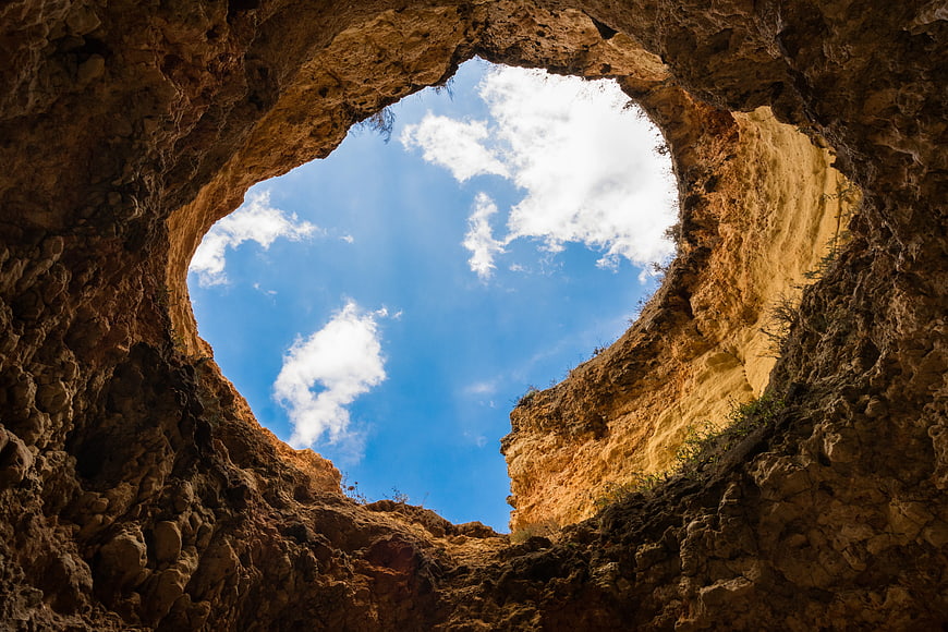 Worm's-eye view of rocky cave opening to blue sky