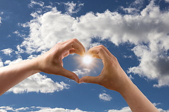 Hands Forming Heart Shape Around Sun in Blue Sky