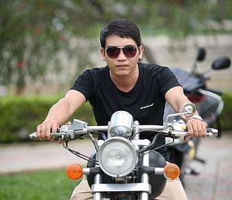 Young Asian man wearing sunglasses riding a motorcycle outdoors