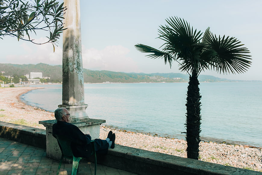 Senior man relaxing on seaside promenade with palm tree