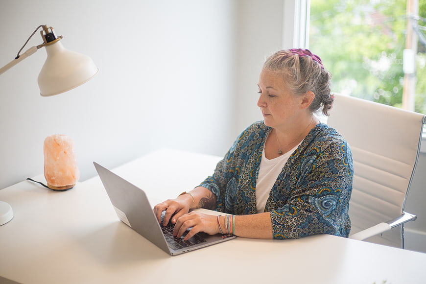Woman working on laptop at white desk with lamp