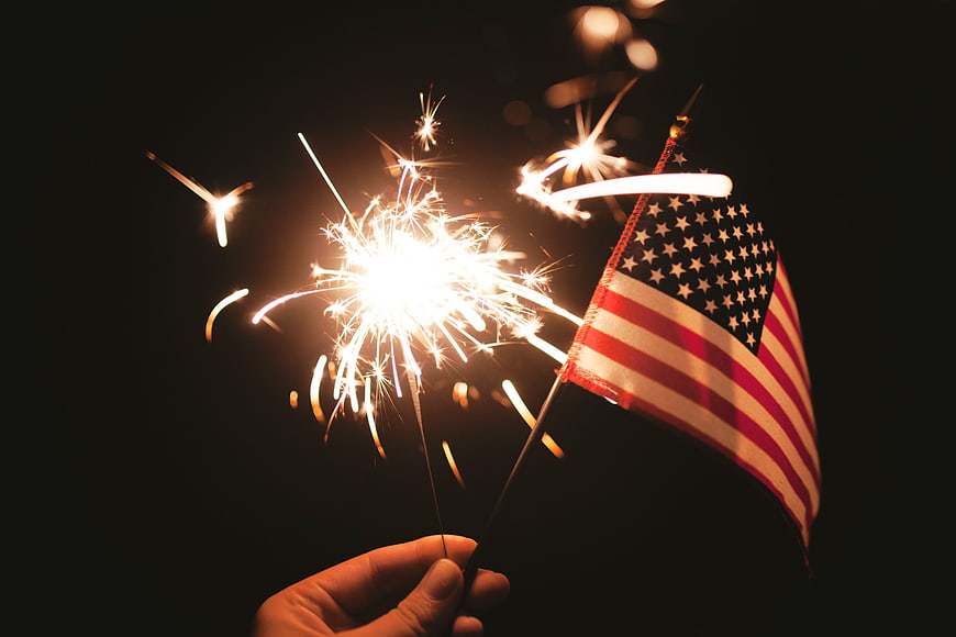 Hand holding sparklers and American flag at night