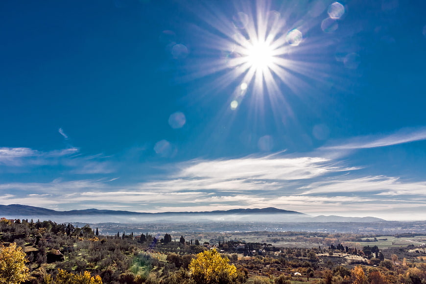 Sunburst over Tuscany landscape with autumn trees and mountains