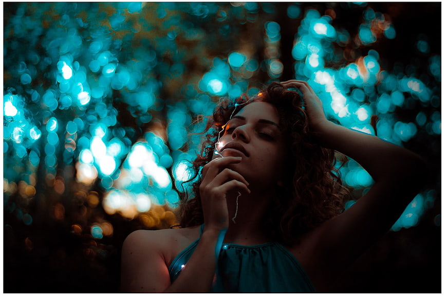 Woman with curly hair in forest with blue bokeh lights