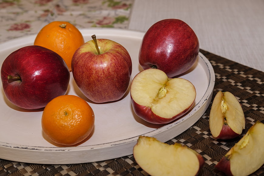 Fresh red apples and oranges on a white plate