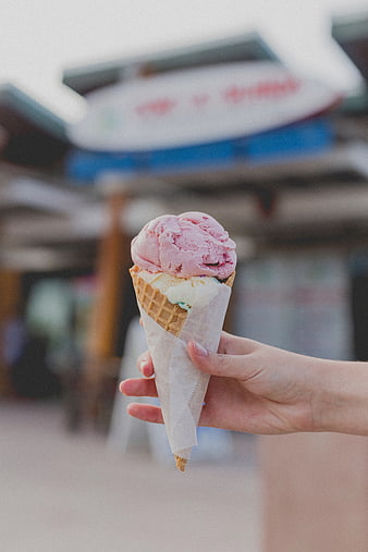 Hand holding pink and white ice cream cone outdoors
