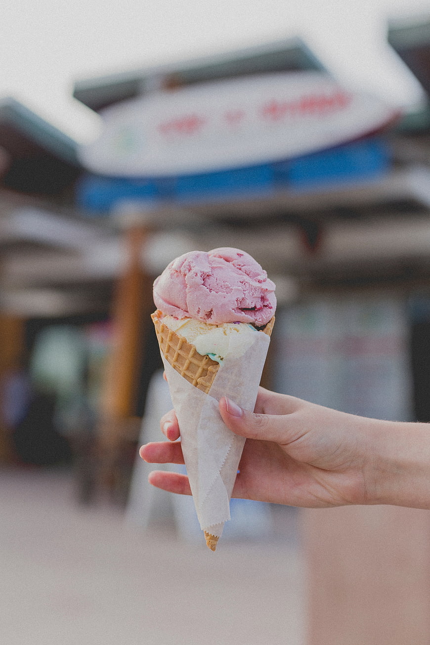 Hand holding pink and white ice cream cone outdoors