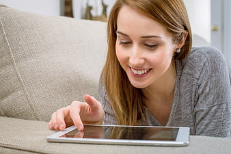 Happy woman using tablet on beige sofa at home