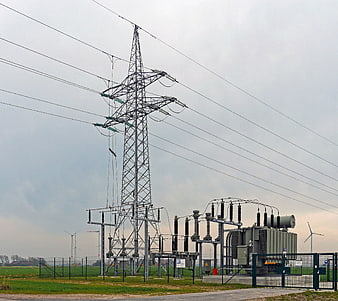 High Voltage Power Substation with Wind Turbines in Background