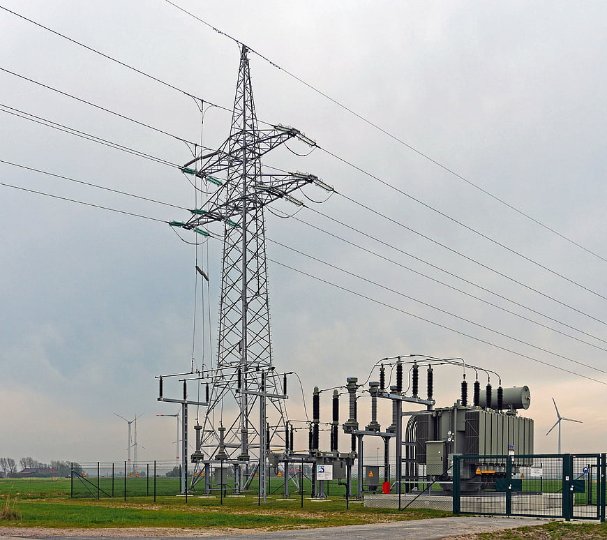 High Voltage Power Substation with Wind Turbines in Background