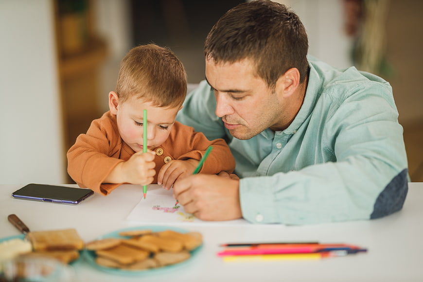 Father and son coloring together at a white table