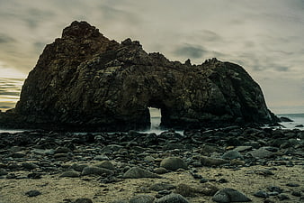 Dramatic Rock Arch on Rocky Beach at Sunset