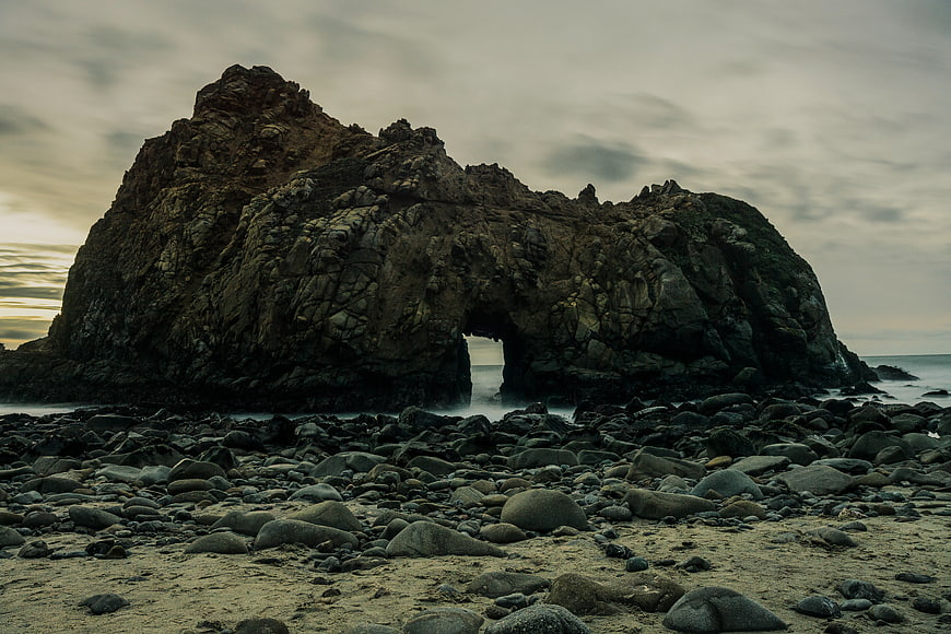 Dramatic Rock Arch on Rocky Beach at Sunset