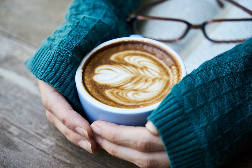 Hands holding latte art coffee cup with book and glasses