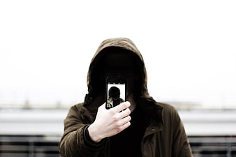 Anonymous hooded figure holding smartphone with face obscured