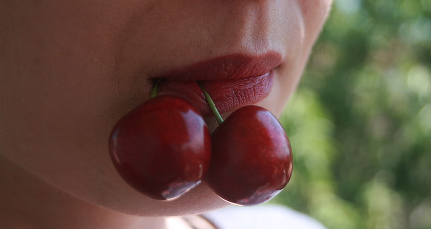 Close-up of woman's lips holding two red cherries