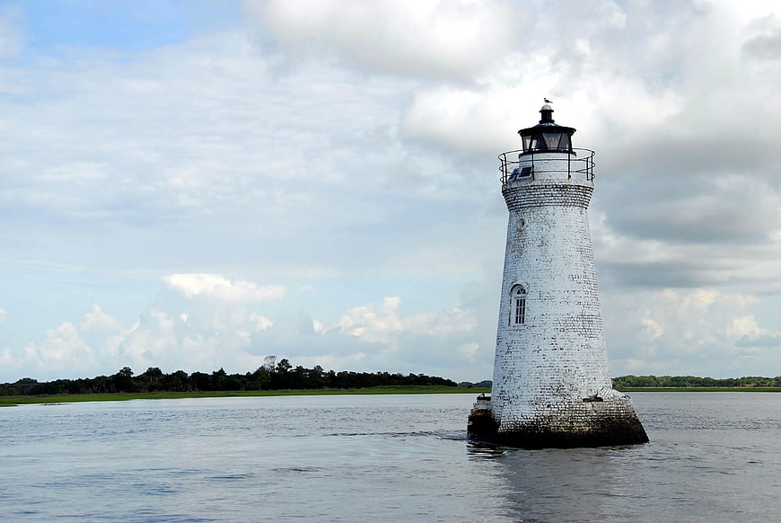 White brick lighthouse standing in calm water under cloudy sky