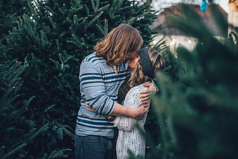 Couple kissing intimately among Christmas trees at dusk