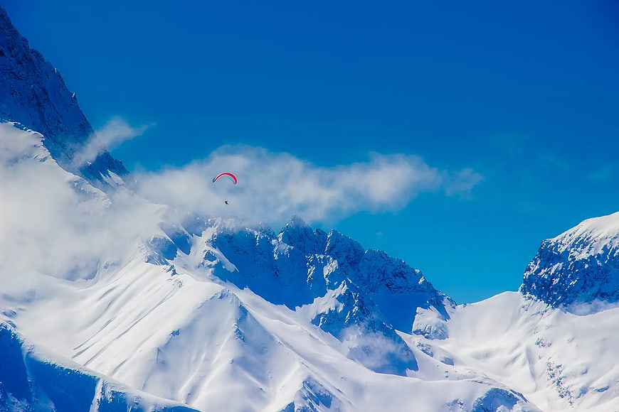 Paraglider soaring over snowy mountain peaks