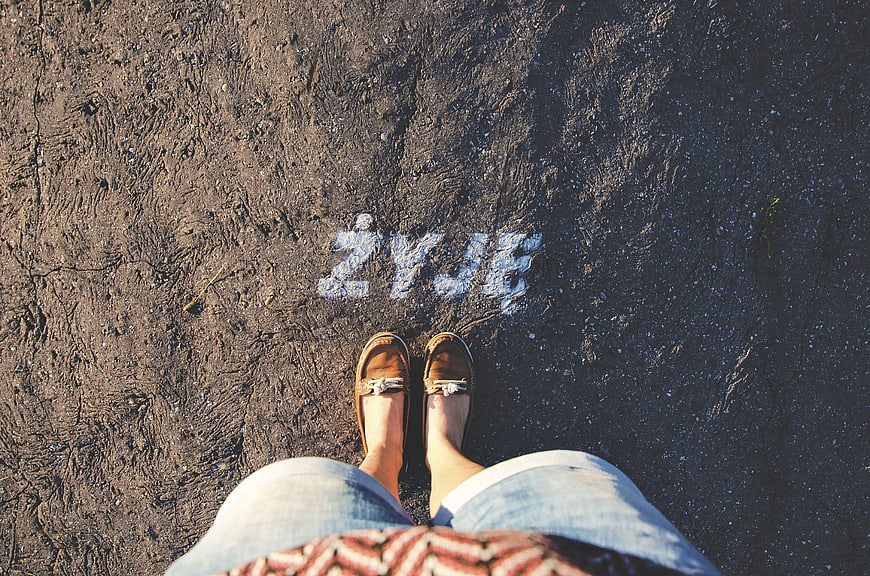 First-person view of feet standing on asphalt with word ZYJE