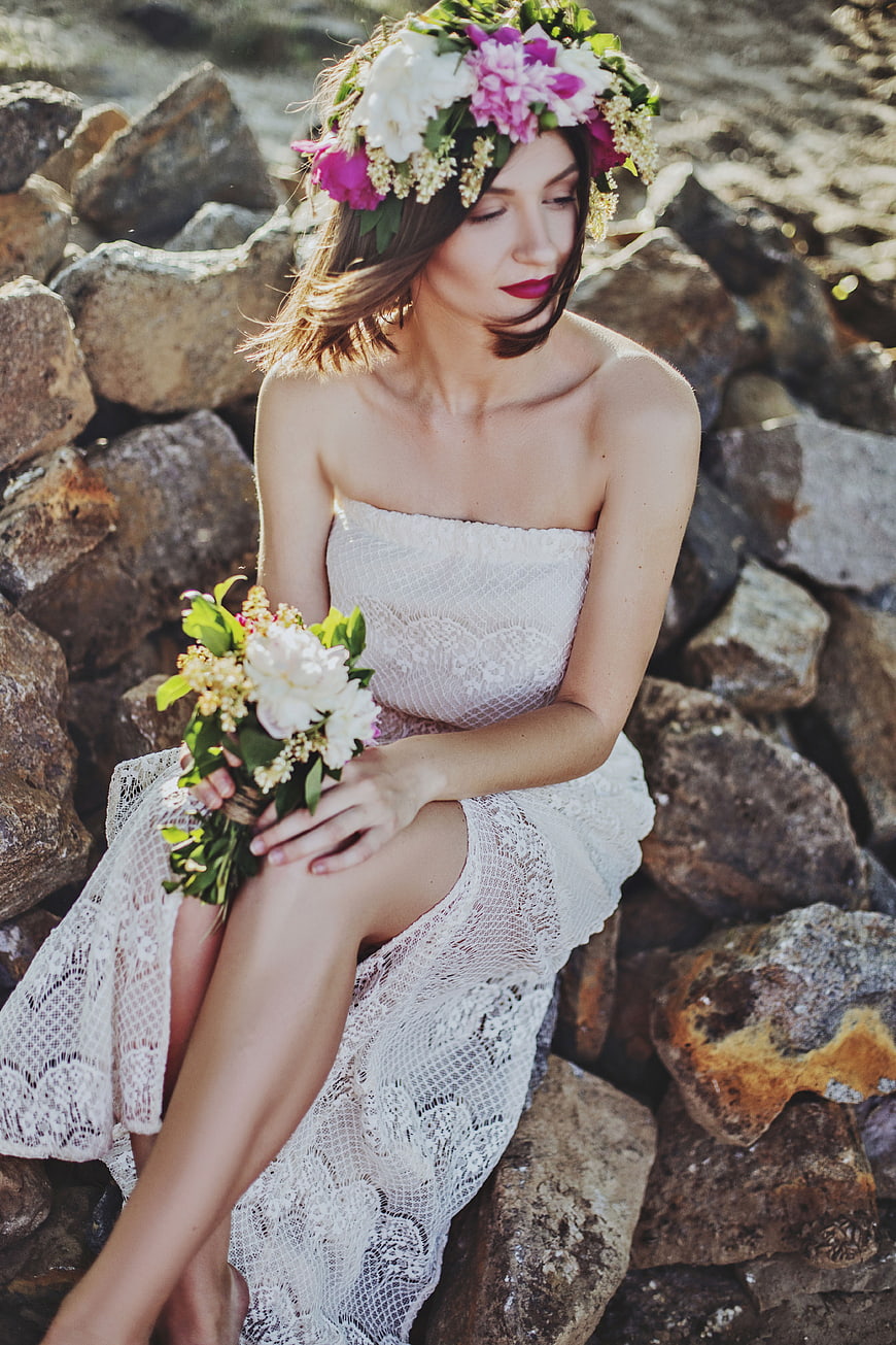 Woman in white lace dress with flower crown on rocks