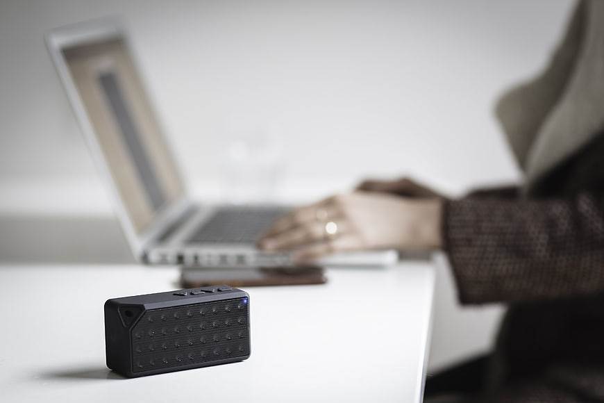 Black Portable Bluetooth Speaker on Desk with Blurred Laptop Background