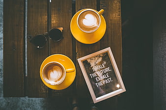 Flat lay of two yellow coffee cups with latte art on wooden table