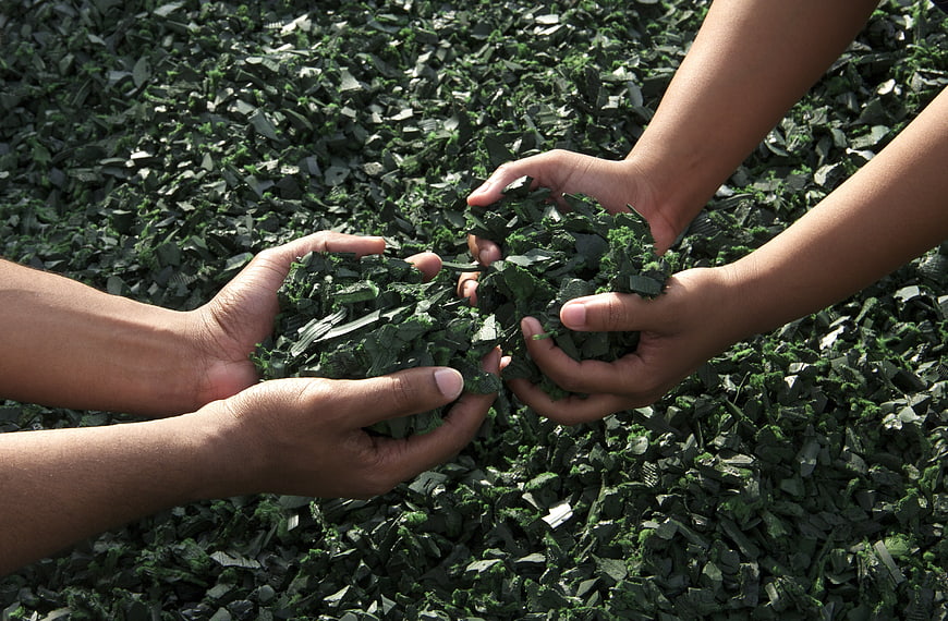 Hands Holding Green Recycled Rubber Shreds Against Textured Background
