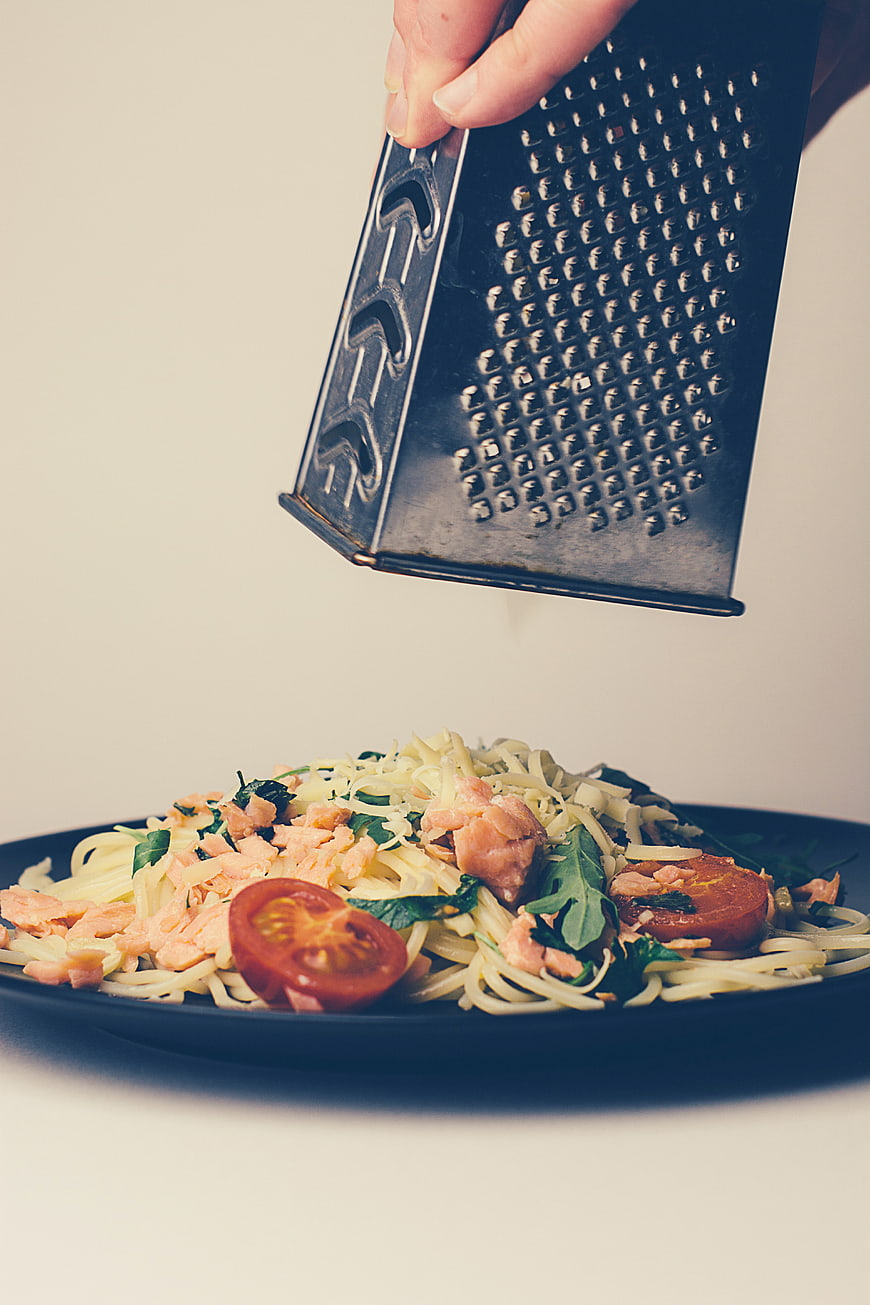 Hand Grating Cheese Over Salmon Pasta Dish
