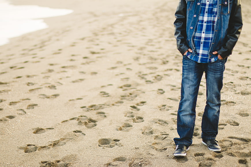 Man in Jeans Standing on Sandy Beach with Footprints