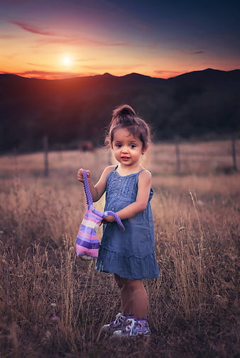 Cute little girl in blue dress holding bag at sunset