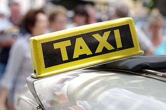Close-up of a yellow taxi sign on a car roof with blurred city background