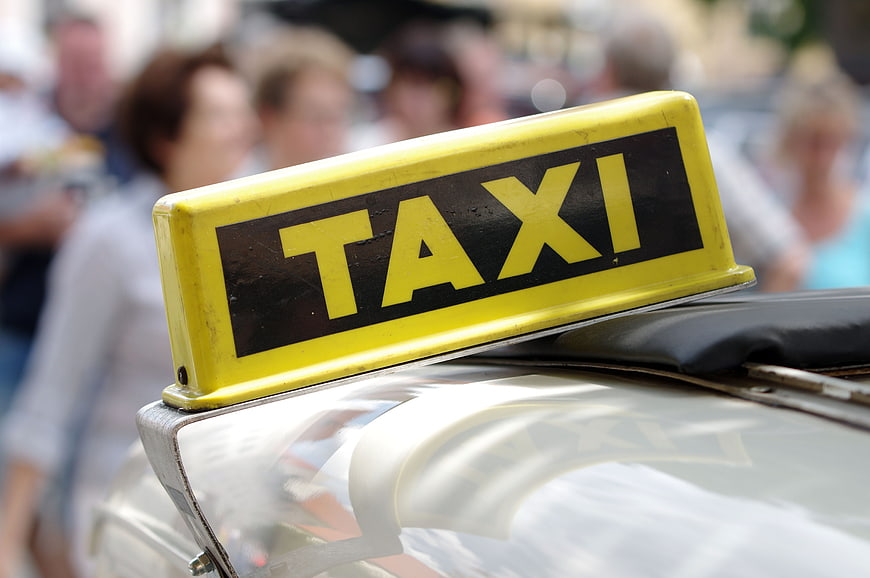 Close-up of a yellow taxi sign on a car roof with blurred city background