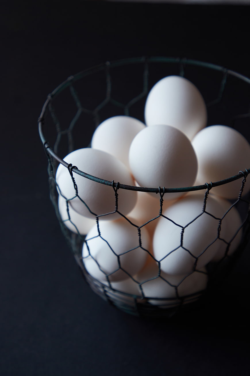 White Eggs in Wire Basket on Dark Background