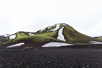 Green mossy mountain with snow patches on black volcanic sand