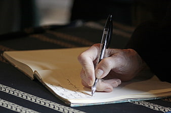 Hand Writing in Notebook with Pen on Dark Table