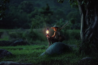 Boy with Lantern Sitting on Rock in Forest at Dusk