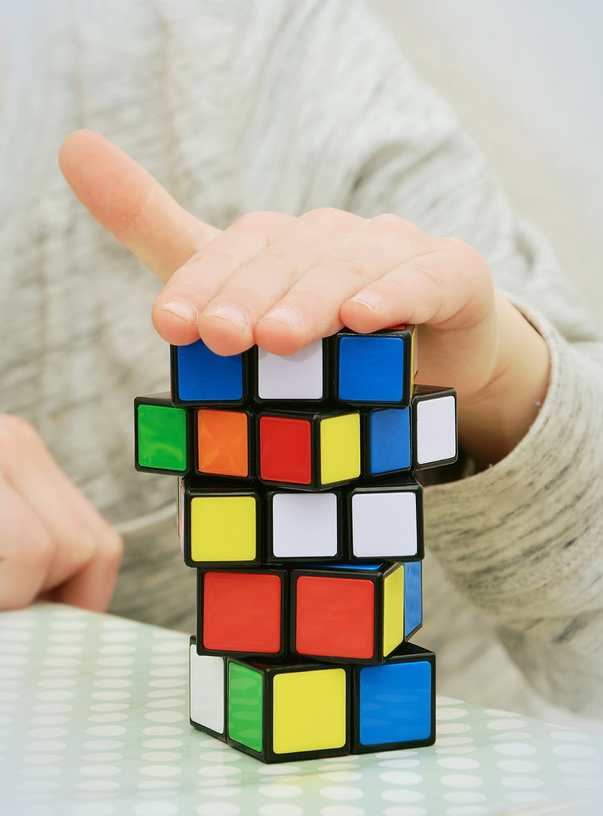 Child's hand balancing tower of Rubik's cubes