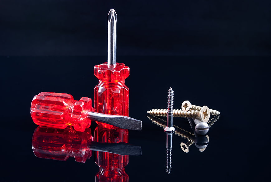 Red Screwdrivers and Assorted Screws on Black Background