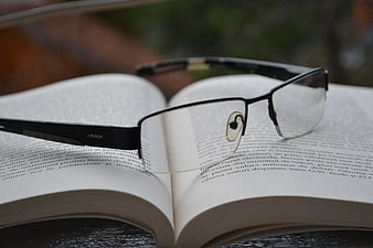 Black Eyeglasses Resting on Open Book Pages