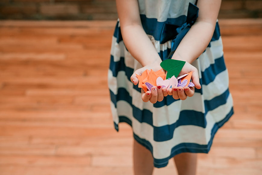 Child holding colorful paper hearts and origami in cupped hands
